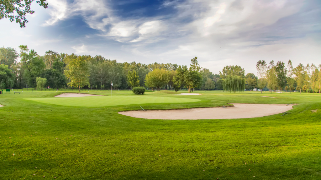 Golf course with sand pit in foreground and trees in background on a sunny day with puffy white clouds in the blue sky