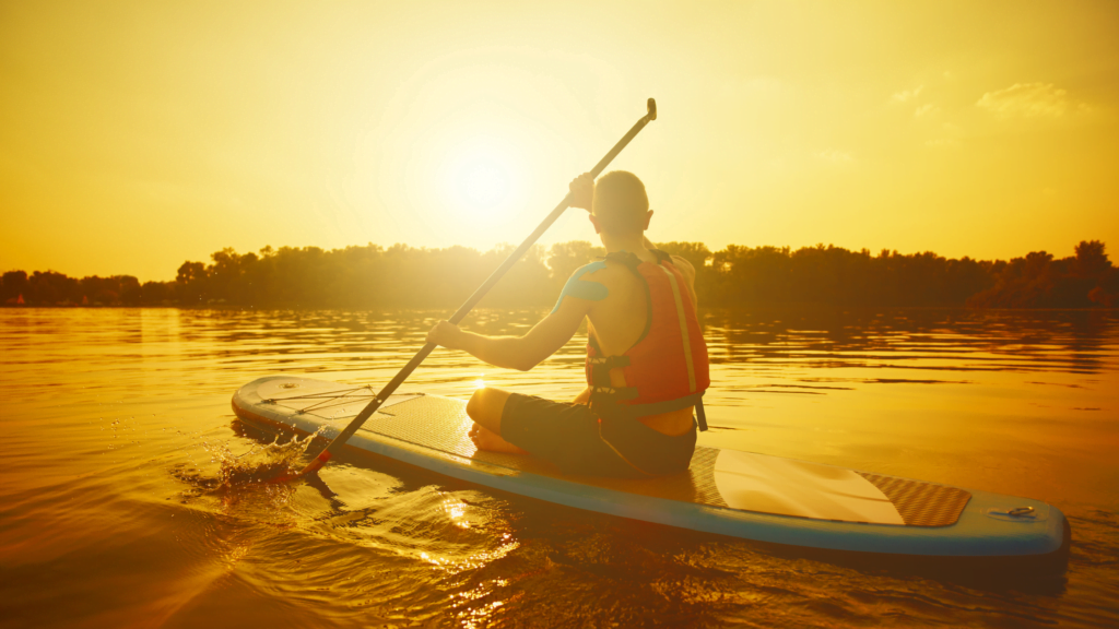 A man on a paddle board in a lake at sunset, staring off into the distance